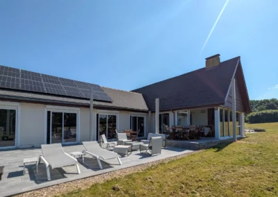 Vue extérieure du gîte le champ de père avec sa terrasse, ses transats et sa grande table en bois
